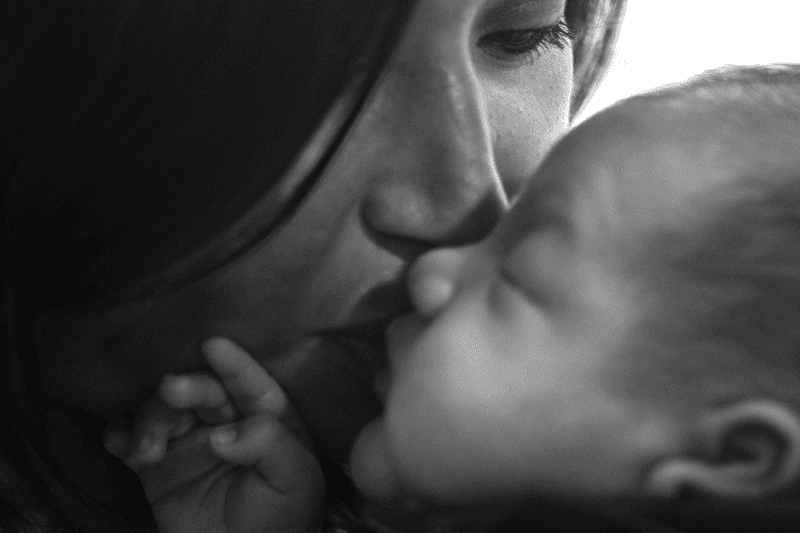Close-up black and grey image of mom kissing newborn baby